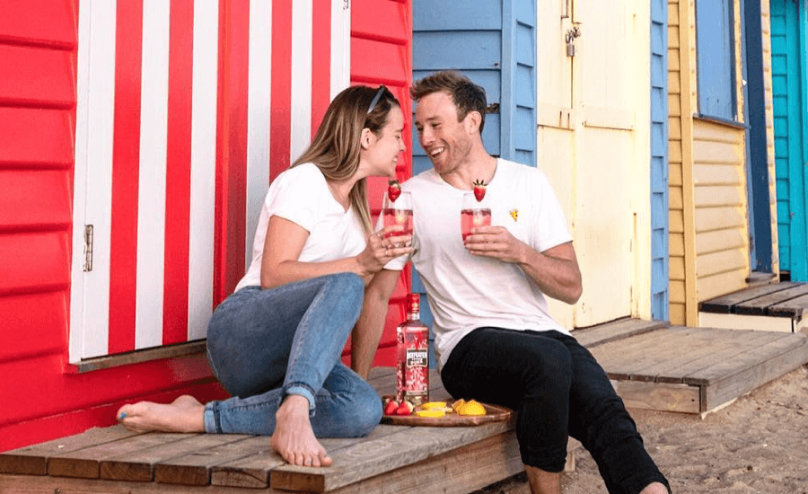 A woman and a man sitting at the beach looking at each other while drinking gin